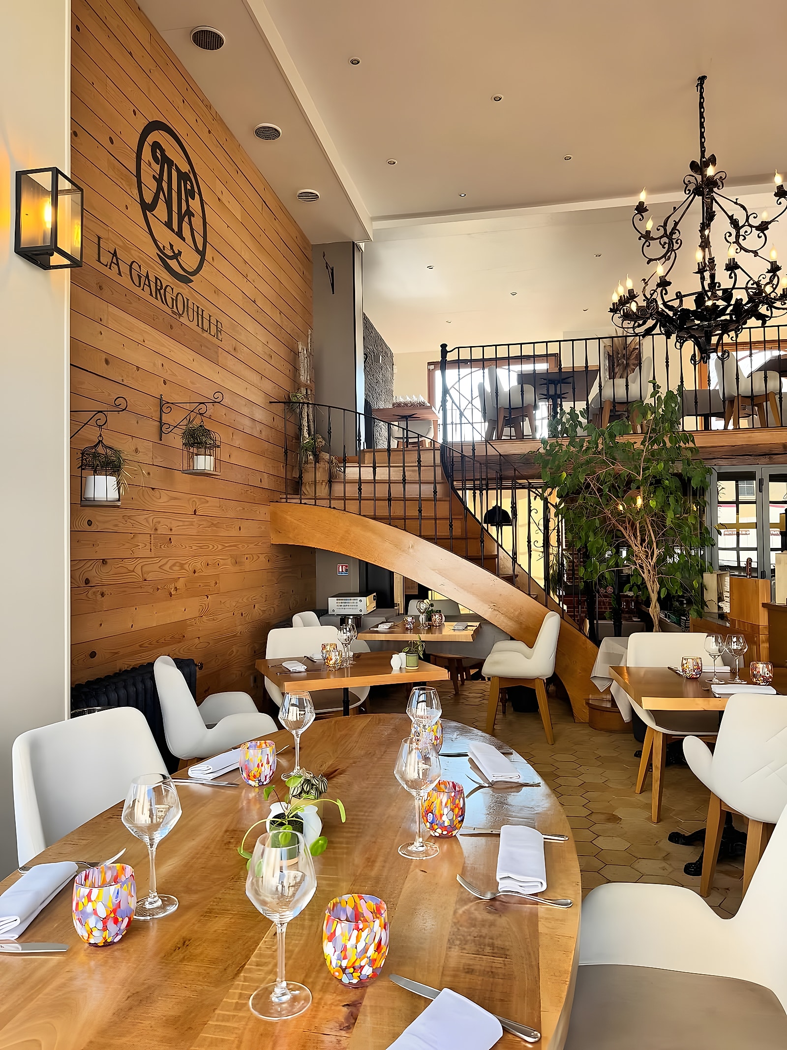 Salle du restaurant La Gargouille à Beauvais : mur en bois avec le logo, escalier, lustre en fer forgé et tables dressées